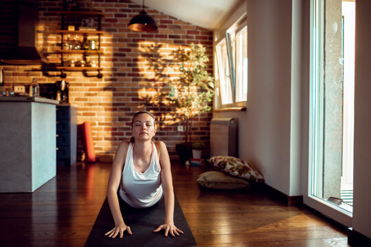 Young woman practicing cobra pose on yoga mat in living room