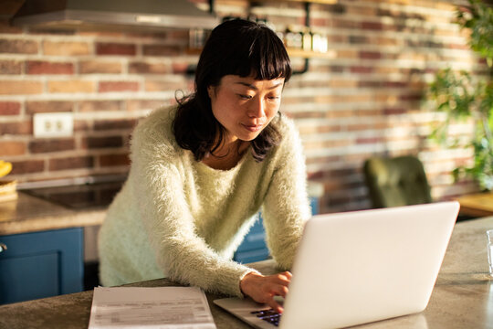 Woman managing finances on laptop in home kitchen