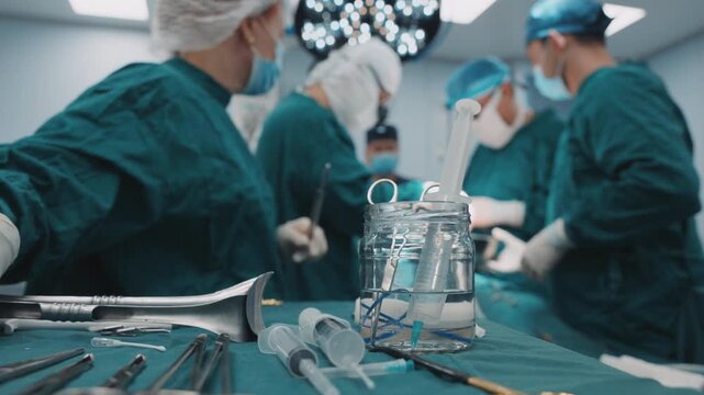 Surgical instruments on operating table while medical team performs procedure in background, healthcare specialists working in sterile operating room during active surgery
