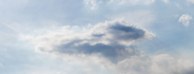 Fototapeta premium Cloudy sky with a large dark gray cloud in the center and light white clouds around, soft daylight, calm atmosphere