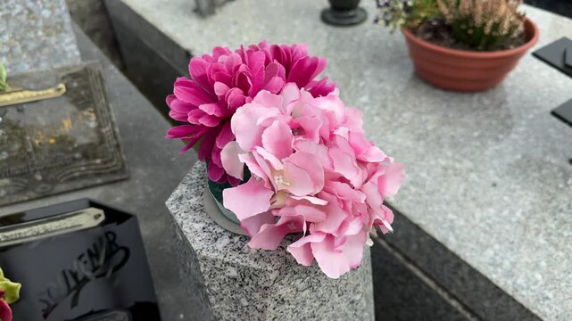Pink artificial funeral flowers on cemetery grave stone