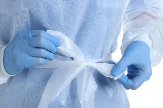 Medical worker tying disposable isolation gown on white background, closeup