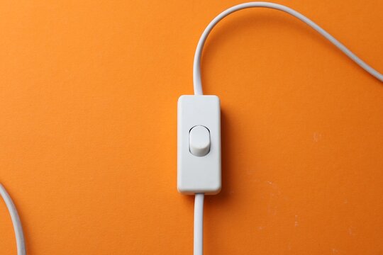 Cord switch for lamp on orange background, top view. Space for text