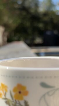 Tracking dolly zoom shot of ceramic mug approaching and revealed on stone pool side ledge in backyard during sunlit morning