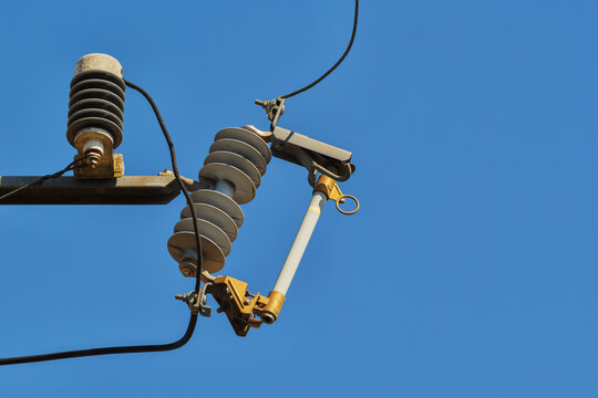 Electrical transformer fuse cutout on a utility pole with ceramic insulators and power lines against a clear sky, representing power distribution and utility infrastructure.
