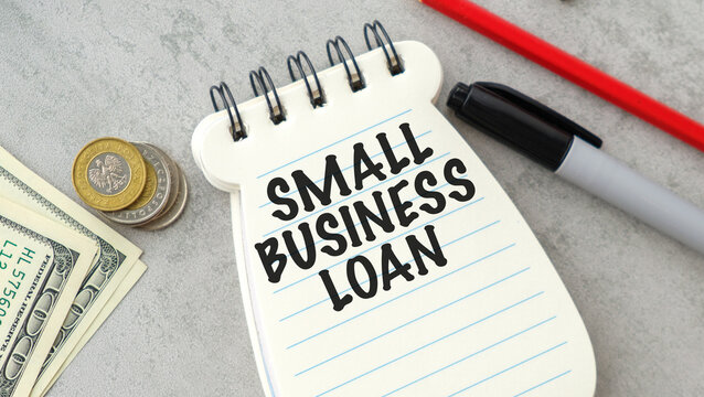 Notepad shows Small Business Loan in bold letters. Coins and bills rest beside the pad on a desk. Red pen and marker lie nearby, ready for use.