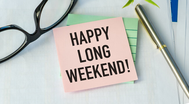 Pink sticky note reads Happy Long Weekend Glasses rest beside it on white surface. Pen and green notepad complete the scene.
