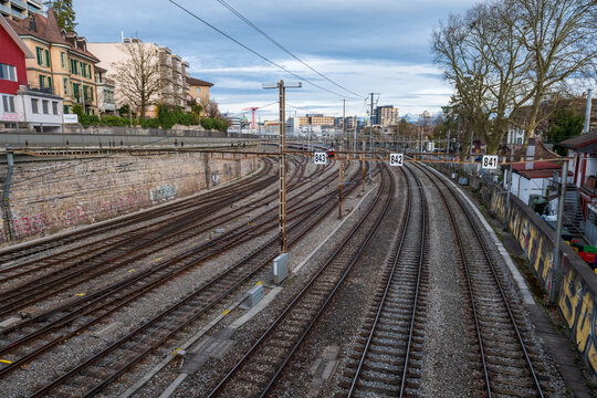 Curving train tracks with catenary wires and urban buildings under cloudy sky in Bern, Switzerland.