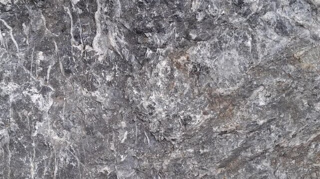Dark grey marble texture with prominent white calcite veins, crystalline structure. Natural stone background. Rugged surface rock featuring intricate geological patterns. Atmospheric mineral texture 