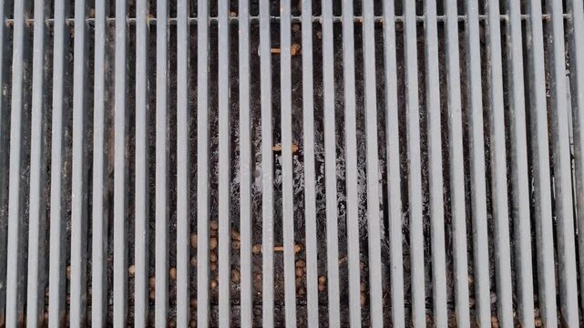 Top-down view of grey metal grate with vertical parallel bars. Urban infrastructure, engineering, architectural. Background featuring rhythmic pattern of grey steel bars on a street drainage system