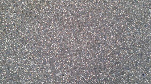 Grey asphalt texture featuring small embedded pebbles. Detailed close-up of dark pavement surface with gritty stone mixture. Durable industrial material choice for city infrastructure, and path 