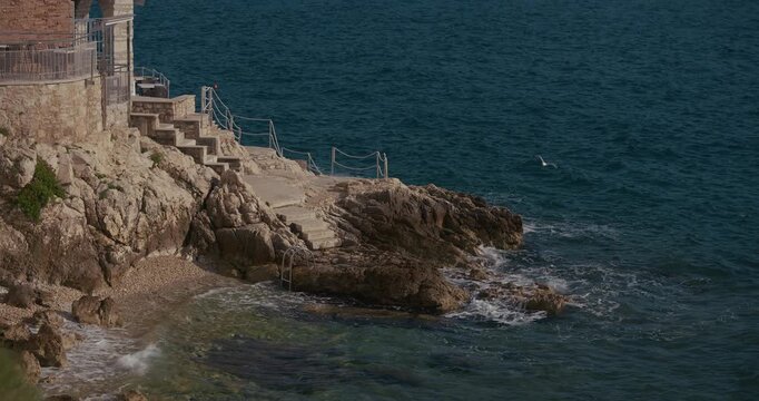Baluota Beach with stone steps and rocky coastline below the Church of St. Euphemia in Rovinj, Croatia during the afternoon.