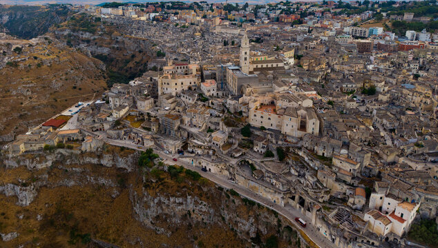 Aerial view of the ancient Sassi di Matera district with its historic stone buildings and cathedral bell tower perched on a rocky cliffside in Matera, Basilicata, Italy.