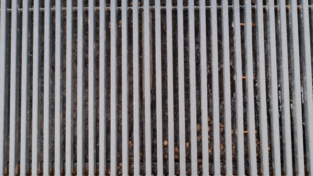 Top-down view of grey metal grate with vertical parallel bars. Urban infrastructure, engineering, architectural. Background featuring rhythmic pattern of grey steel bars on a street drainage system