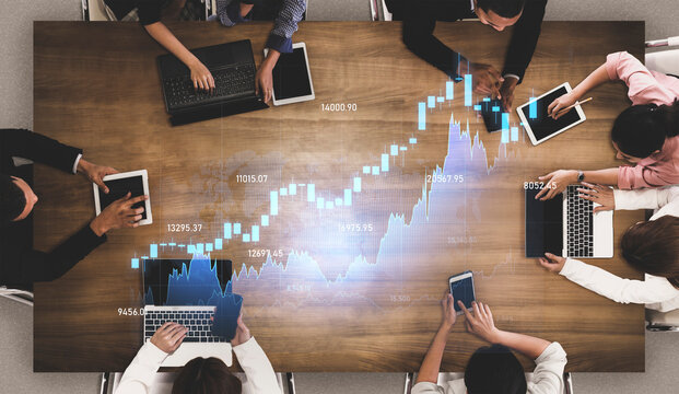 Aerial view of diverse professionals collaborating over stock market data, utilizing laptops and tablets in a modern office, showcasing teamwork and technology. Scalp