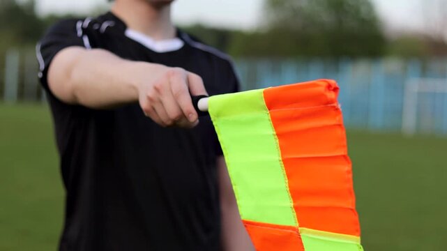 Assistant referee in black uniform holding a linesman flag on a soccer field, signaling during a match. Concept of officiating, rules enforcement, fair play and game control in football.