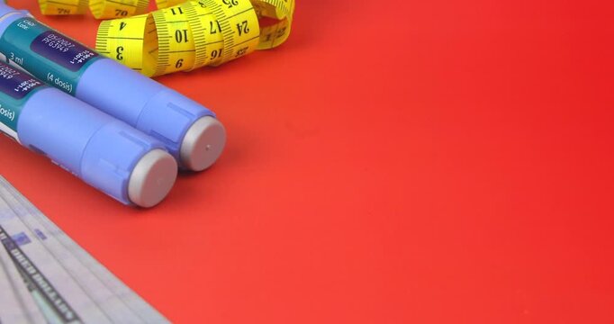 Blue semaglutide GLP-1 pens for weight control and a yellow measuring tape on a red gradient background during a camera panning shot.