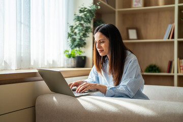 Obraz premium Woman working remotely on laptop from a comfortable home sofa