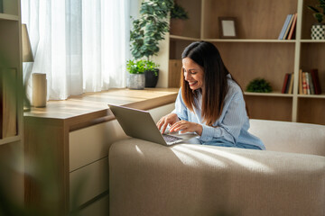 Obraz premium Smiling woman using laptop for remote work at home