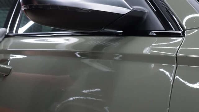 The process of applying a nano-ceramic coating for hydrophobic effect on the green car's hood by a male worker with a sponge and bottle of chemical composition and microfiber. Auto detailing service. 