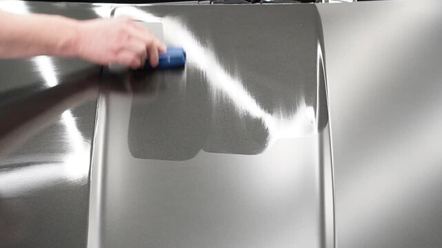 The process of applying a nano-ceramic coating for hydrophobic effect on the grey matte car's hood by worker with a sponge, bottle of chemical composition, microfiber. Auto detailing service industry.