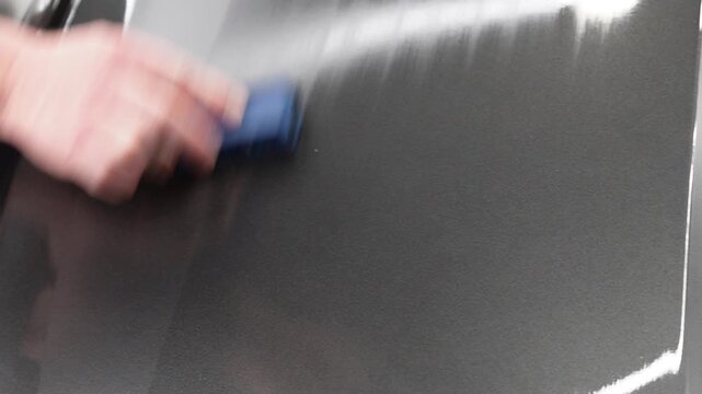 The process of applying a nano-ceramic coating for hydrophobic effect on the grey matte car's hood by worker with a sponge, bottle of chemical composition, microfiber. Auto detailing service industry.