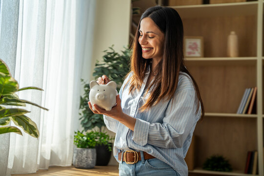 Woman smiling while putting money into piggy bank