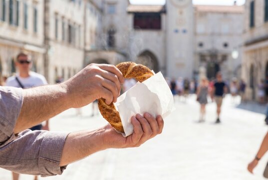 Holding a fresh sesame simit bread in a paper wrapper on a sunny city street