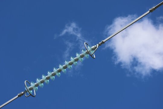 Detailed view of a modern high‑voltage power line tower against a clear blue sky with bright sunlight and scattered cumulus clouds, showcasing contemporary Swedish energy infrastructure.