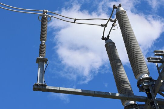Detailed view of a modern high‑voltage power line tower against a clear blue sky with bright sunlight and scattered cumulus clouds, showcasing contemporary Swedish energy infrastructure.