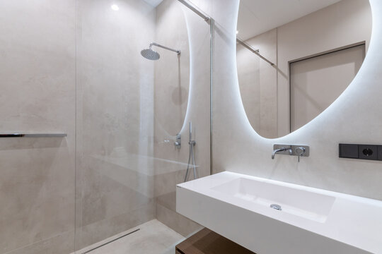 The bathroom is decorated in pastel colors. Shower behind a glass partition. The mirror is illuminated.