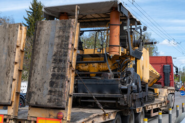Fototapeta premium Asphalt paver is loaded on a truck and prepared for road work at a construction site under blue sky during daylight hours