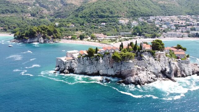 Aerial 4K drone view of Sveti Stefan island from the sea, Montenegro, featuring turquoise waters, lush nature, and scenic coastal beauty