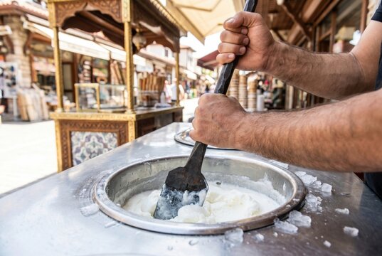 Vendor hands using a long metal tool to churn traditional thick sticky ice cream in a metal vat