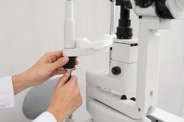 Naklejka premium Optometrist hands adjusting a white slit lamp eye examination machine in a clinic