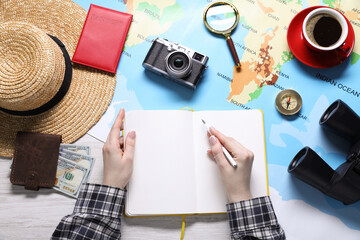 Fototapeta premium Woman with notebook and world map planning trip at wooden table, top view
