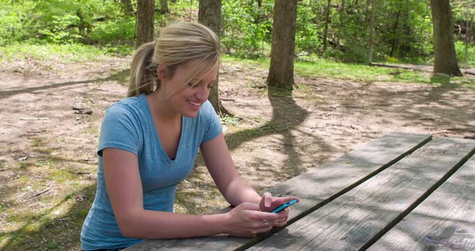 Girl sitting at bench in woods texting 4k
