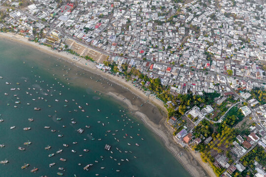 Aerial view of Mui Ne Beach featuring numerous traditional fishing boats anchored in the turquoise water along the dense coastal urban settlement Thanh pho Phan Thiet, Binh Thuan, Vietnam.