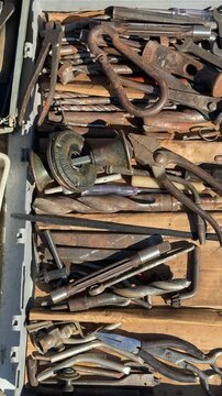 Secondhand tools on asphalt flea market, rusty pliers, wrenches, drill bits, wire cutters and sockets arranged in worn wooden