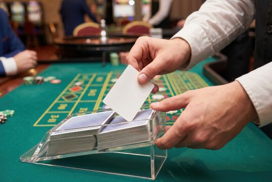 Casino dealer pulling a playing card from an acrylic dealing shoe on a green felt table