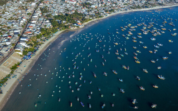 Aerial view of Mui Ne Beach with traditional round coracles and fishing boats scattered across the blue water near the coastal village in Phan Thiet, Binh Thuan, Vietnam.