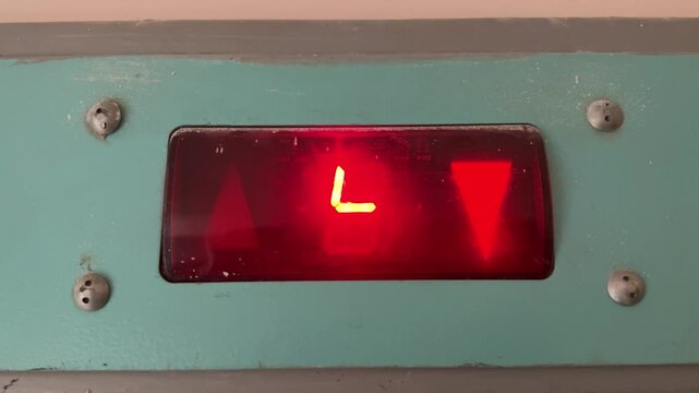 Red diode elevator indicator shows movement, flashing arrow and digits across teal metal panel, exposed screws and worn paint