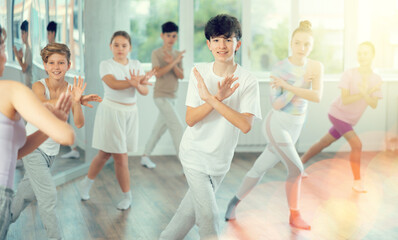 Naklejka premium Guy teen performs modern dances repeats movements of unrecognizable teacher together with friends during lesson at choreographic school. Hobbies, active pastime