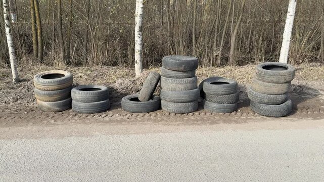 Stacked worn tires on gravel roadside. Birch trees background, columns of passenger car tires awaiting collection, weathered