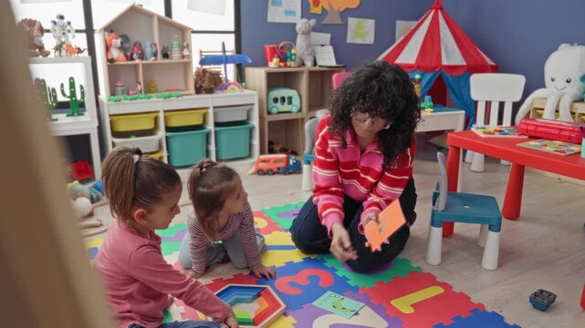 Teacher shows flashcards and points while girl touches chin on colorful foam mat in preschool classroom; curiosity learning.