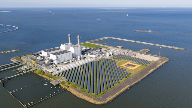 Aerial view of the Maxima Power Plant featuring rows of solar panels and industrial chimneys on the coast of the Markermeer in Lelystad, Flevoland, Netherlands.