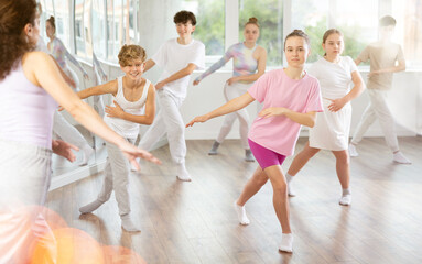 Naklejka premium Female teacher performs choreographic exercises and teaches energetic mobile social house dance together with teenagers