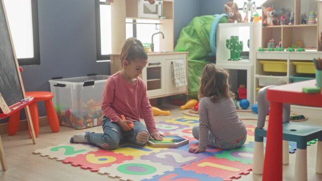 Two girls play with a shape puzzle on a foam number mat, one hand placing a wooden tile beside toy blocks in a building; joyful learning.