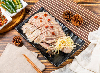 Fototapeta premium A black plate of sliced meat with red peppers and shredded vegetables on a wooden table with napkins and chopsticks