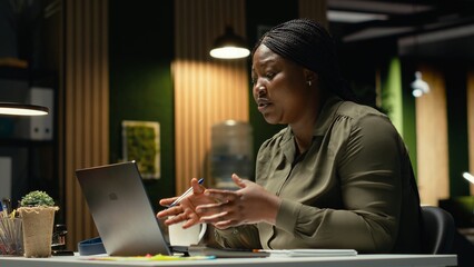 Black businesswoman greeting people on a video call network at office smiling, hosting a briefing meeting. Engaging in a virtual conversation, exchanging ideas about successful enterprise. Camera B. © DC Studio